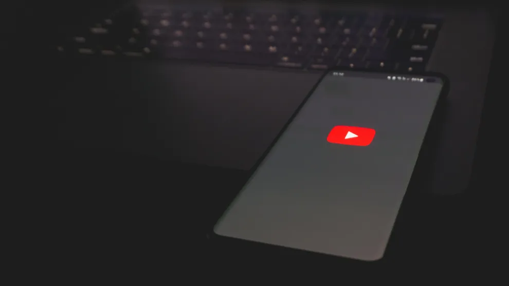 Smartphone auf einem Laptop abgelegt. Auf dem Bildschirm des Smartphones wird das YouTube Logo dargestellt.